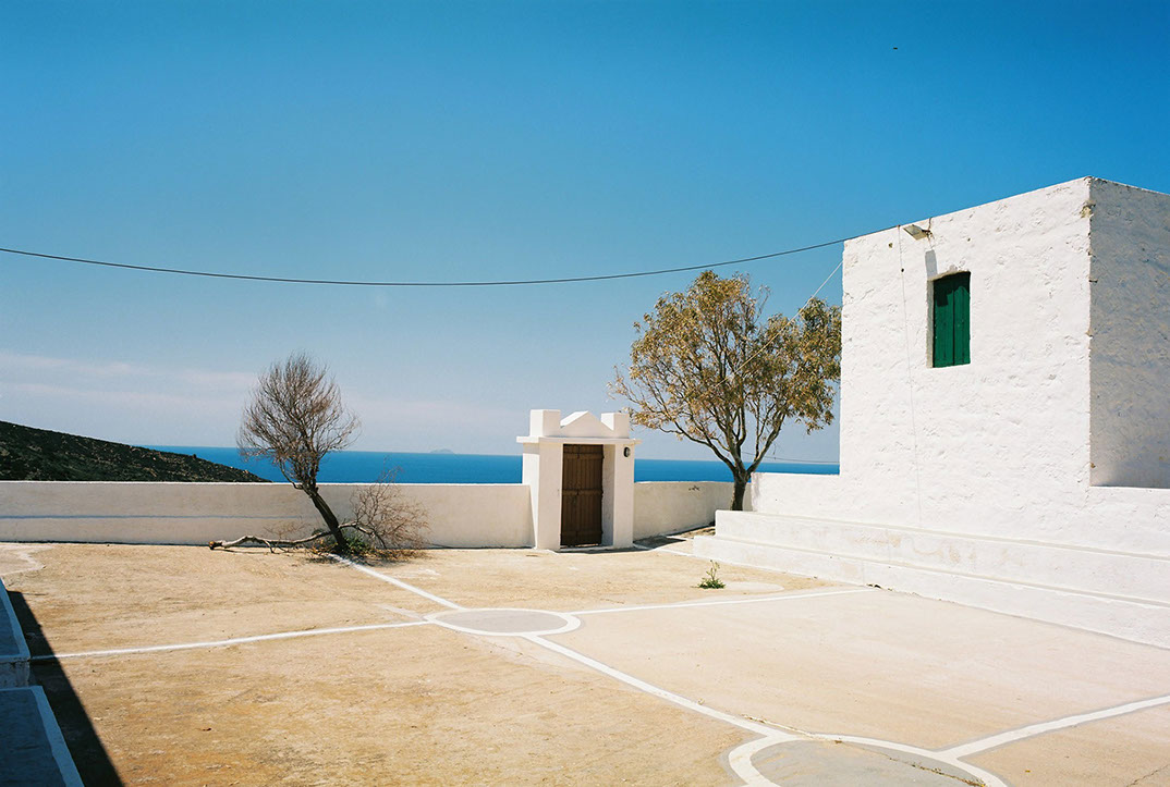 Vue d'une partie du monastère d'Agios Ioannes, avec 2 arbres et en fond la mer Egée