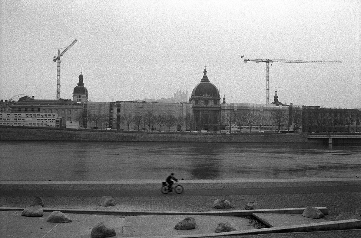 Photographie de rue montrant un matelas et quelques affaires appartenant à un SDF à Lyon, avec en perspective 2 hommes de dos discutant